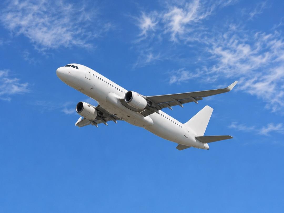 A white twin-engine passenger jet climbing against a blue sky with light clouds