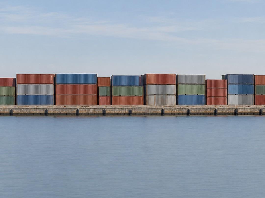 Stacked shipping containers on a quay seen across calm harbour water