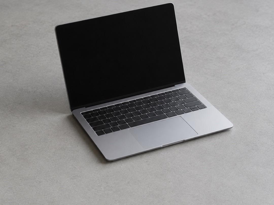 Thin silver laptop, half open with a dark screen, on a light grey concrete surface